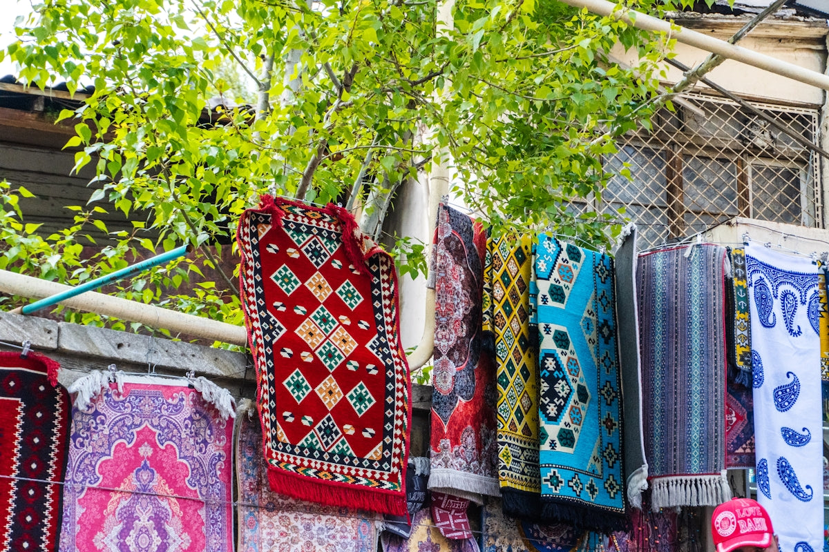 Colorful rugs and textiles displayed outdoors with greenery